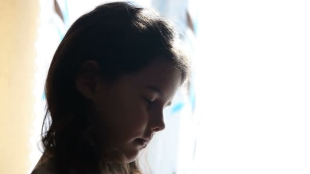 Девочка ребенок молится стоя у окна силуэт Видео религия детства — стоковое видео