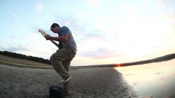 남자 음악가 자연 호수 재생 비디오를 설정 하는 태양 전기 기타 저녁 근처 일몰에 옆으로 서 — 비디오
