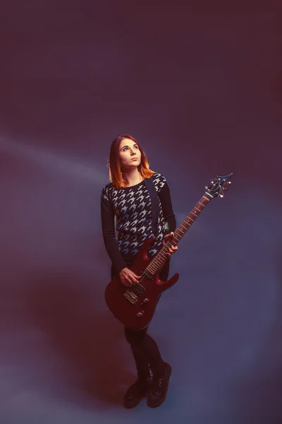 Menina de aparência europeia em uma camisola segurando uma guitarra e olhando — Fotografia de Stock