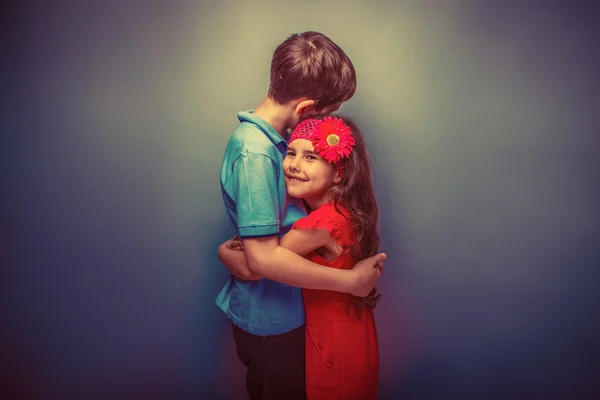Teenager Mädchen umarmt einen Teenager Jungen auf einem grauen Hintergrund retro — Stockfoto