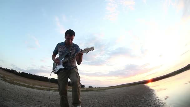 Gatumusikant börjar att spela elgitarr i solnedgången solen går ner floden Video — Stockvideo