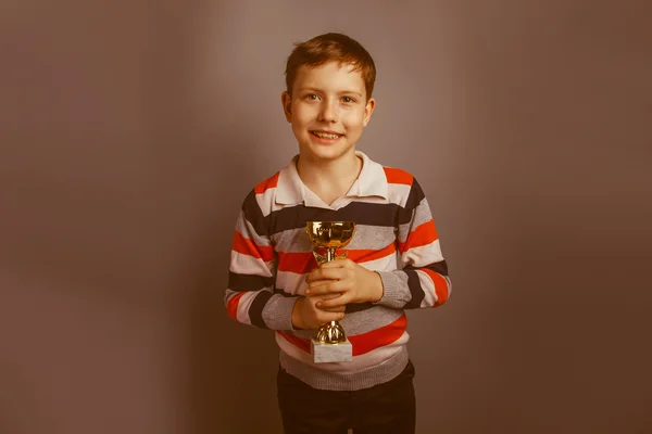 Niño de aspecto europeo de diez años sosteniendo un premio de copa en un gris —  Fotos de Stock