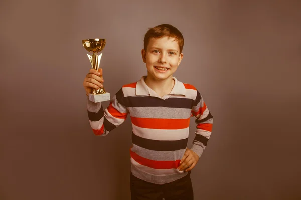 Niño de aspecto europeo de diez años sosteniendo un premio de copa en un gris —  Fotos de Stock