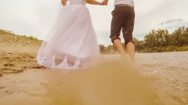 Junges Paar Braut und Bräutigam läuft durch das Wasser Blick vom hinteren Fuß sprühen große Tröpfchen Wasser Hochzeit — Stockvideo