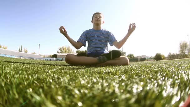 Teenager sitting  boy meditating yoga stadium grass green summer — Stock Video