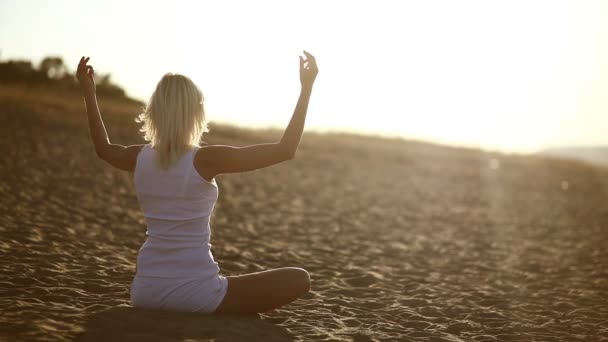 Woman in white sitting on sand meditation healthy lifestyle sunset the sun goes down, silhouetted against the sky Yoga — Stock Video