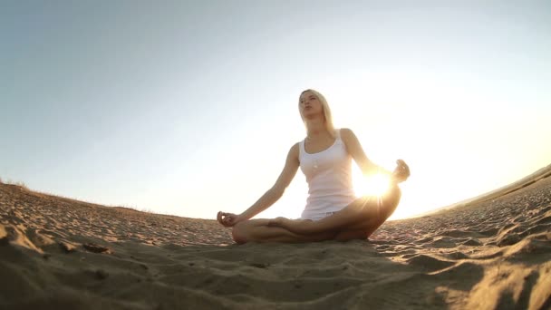 Mujer en blanco sentada en la arena meditación estilo de vida saludable puesta de sol el sol se pone, silueta contra el cielo Yoga — Vídeo de stock