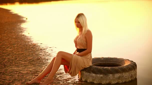 Sexy young  seductive portrait girl woman dress develops on sunset yellow desert sand walking slowly dress He is sitting on a car tire — Stock Video