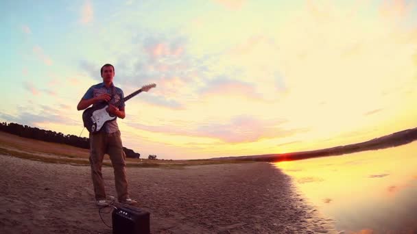 Gitarist muzikant man stopt de elektrische gitaar spelen op de rivier en vertrekt avondrood wolken reflectie kleur — Stockvideo
