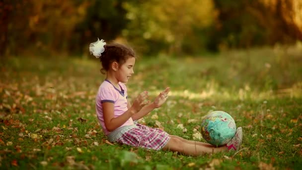 Брюнетка-подросток, сидящая на зеленой траве и изучающая глобус — стоковое видео