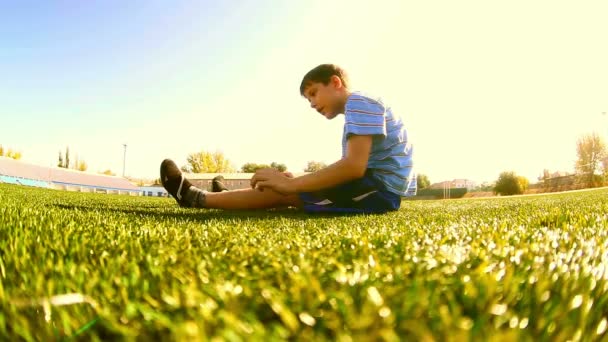 Adolescente fazendo menino treino de futebol atleta senta-se em uma ginástica esportiva grama — Vídeo de Stock