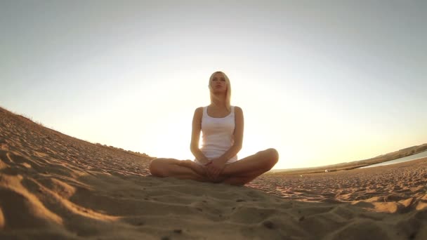 Szőke nő ült a homokon a sivatagban, egészséges életmód jóga meditáció fehérbe öltözött — Stock videók