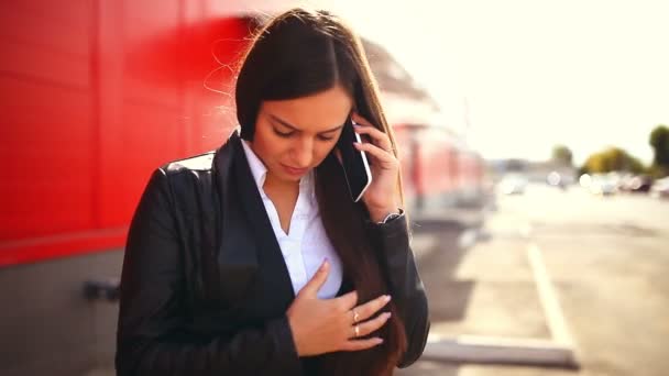 Brunette meisje in straat praten over de telefoon lachende vrouw achter de buiten rode achtergrond — Stockvideo