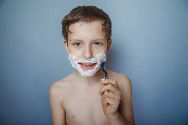 Boy  teenager European appearance   shaves face on a gray — Stok fotoğraf