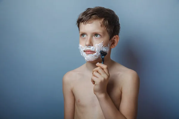 Boy  teenager European appearance shaves face on a gray — Stock fotografie