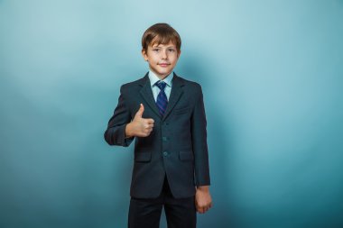 European appearance teenager boy in a business suit shows a sign