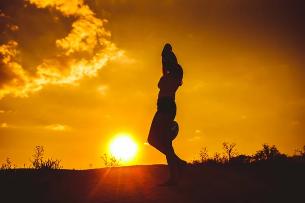 Silhouette of a young girl in a shirt and shorts holds over his — Stock Photo, Image