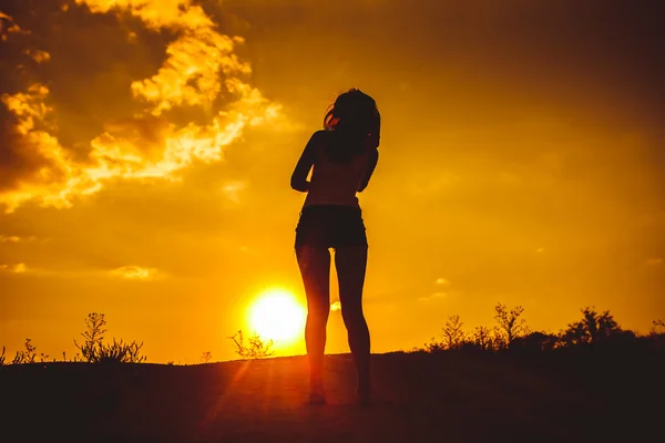 Silhouette of a young girl in t-shirt and shorts looking at the — 图库照片