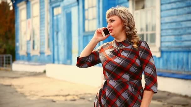 Толстая толстая женщина среднего возраста разговаривает по телефону на голубом фоне старый дом образ жизни — стоковое видео