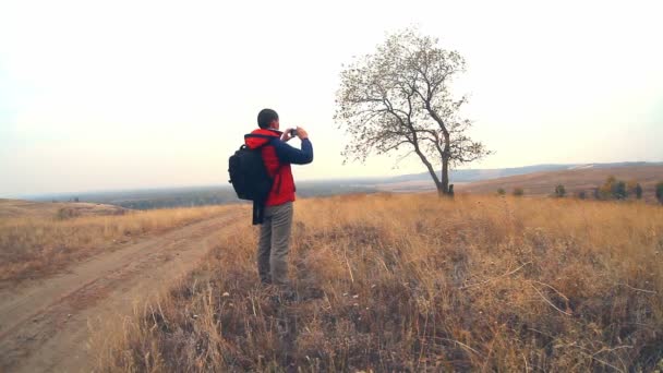 Hiker man traveler with a backpack in the autumn is on the way to nature is a solitary tree travel — Stock Video