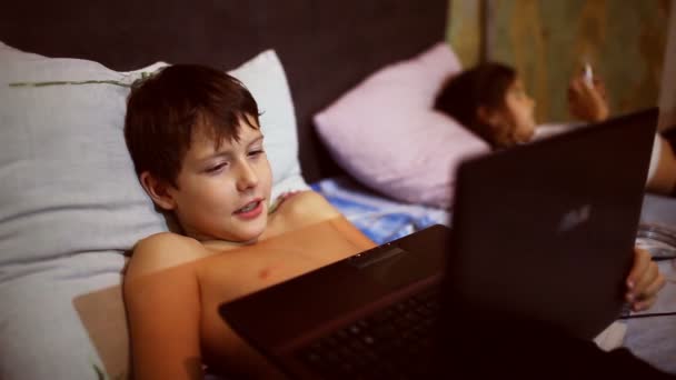 Dospívající dítě chlapec hraje počítačové hry přenosný notebook leží v posteli večer — Stock video