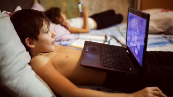 Nastoletni dzieciak chłopiec gry komputerowe gry laptopa notebooka leżącego w łóżku w wieczór — Wideo stockowe