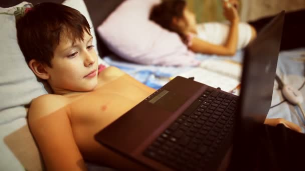 Подросток играет в компьютерные игры ноутбук мальчик лежит в постели вечером — стоковое видео