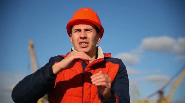 Turuncu kask bir adam üreticisi portresi çağıran bir mavi gökyüzü ve inşaat karşı sallayarak bağırır