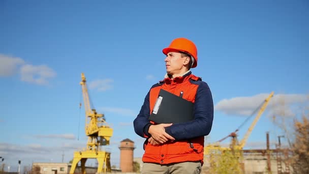 Builder mannen i en hjälm korrigerar orange mot den blå himlen och en kran — Stockvideo