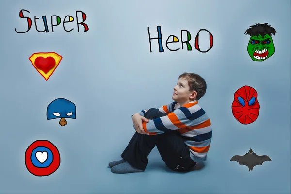 Мальчик сидит на полу и смотрит вверх улыбающийся супергерой супер — стоковое фото
