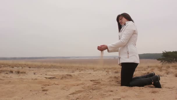 Vrouw knielt en gooit zand herfst koude natuur — Stockvideo