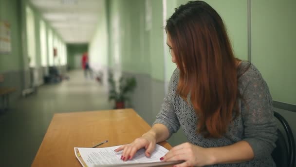 Vrouw leraar controleert huiswerk zitten aan een bureau in school hal — Stockvideo
