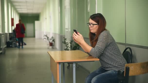 Nő girl gazdaság smartphone intelligens telefon keresés-az internet iskolai ülő folyosón — Stock videók