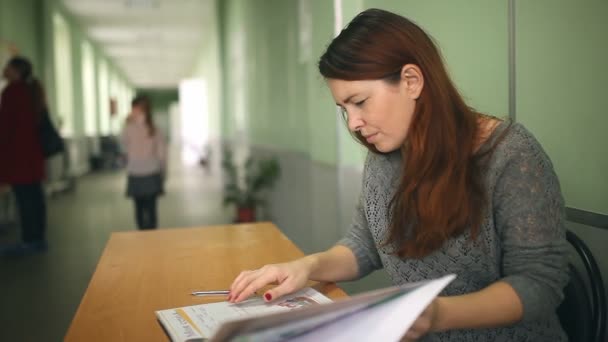 Profesora comprueba la tarea sentada en el pasillo de la escuela — Vídeo de stock