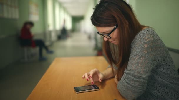 Kvinna tjej håller smart phone Sök i smartphone internet skolan sittande korridor — Stockvideo