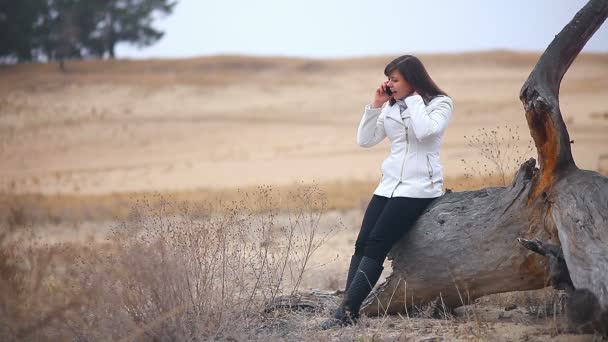 Girl woman talking on the phone sitting on a dry log autumn nature — Stock Video
