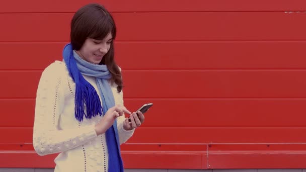 Mujer niña sosteniendo un teléfono inteligente en una chaqueta y una bufanda redes sociales medios de comunicación — Vídeo de stock