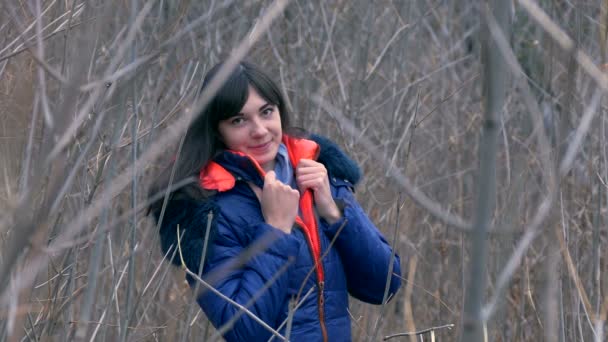 Vrouw meisje in jas en een sjaal staande in de droge takken van jonge bomen — Stockvideo