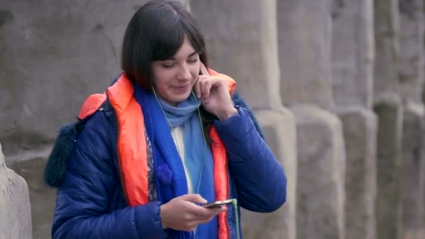 Nő lány hallgat zenét okostelefon fejhallgató kabát és egy sál — Stock videók