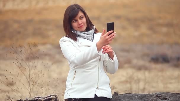 Teléfono inteligente mujer niña hace auto teléfono sentado en un árbol seco naturaleza de otoño — Vídeos de Stock