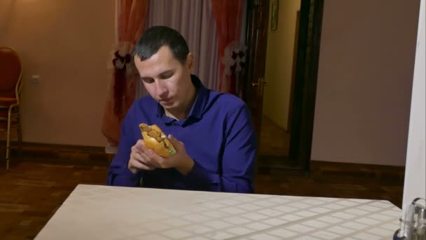 Hombre comiendo una hamburguesa comida rápida sentado en el café — Vídeos de Stock