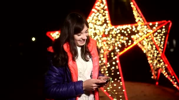 Femme fille écoute de la musique sur votre téléphone avec écouteurs la nuit sur fond étoiles bokeh — Video