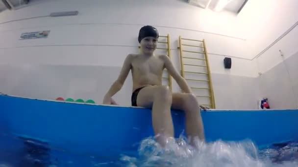 Dospívající chlapec sedí na okraji bazénu šplouchání vody nohy — Stock video