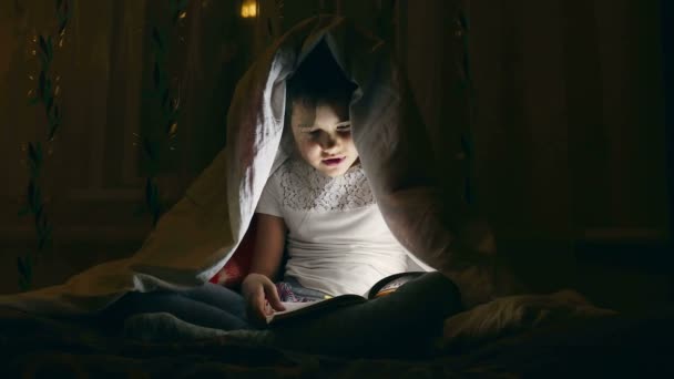 Girl reading a book with a flashlight under the covers at night — Stock Video