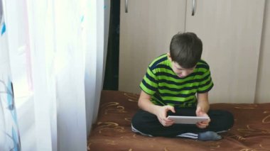 Genç çocuk içinde bir kanepede oturan tablet oynarken