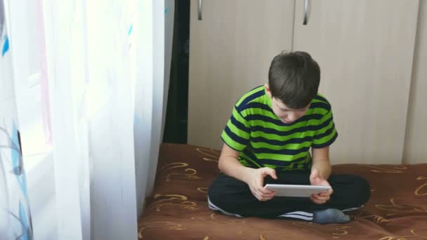 Teenager spielt auf dem Tablet sitzend auf einer Couch in — Stockvideo