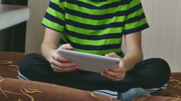 Хлопчик підліток грає на планшеті, сидячи на дивані — стокове відео