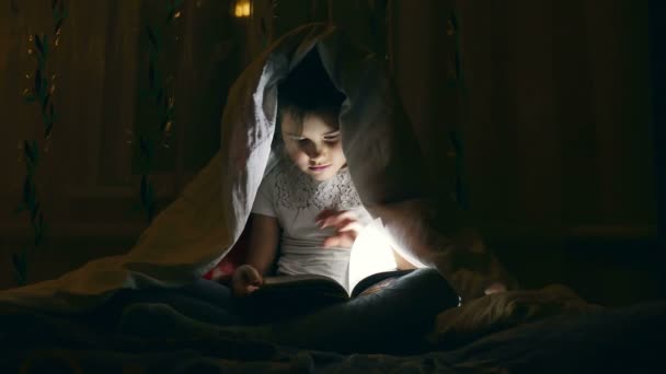 Chica leyendo libro con una linterna debajo de las cubiertas en la noche — Vídeos de Stock