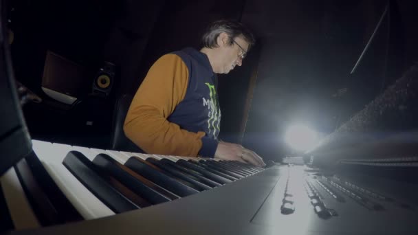 Музыкант сидит в студии на синтезаторе — стоковое видео