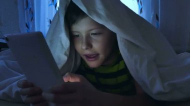 Tablet gece battaniyenin altında oynayan çocuk